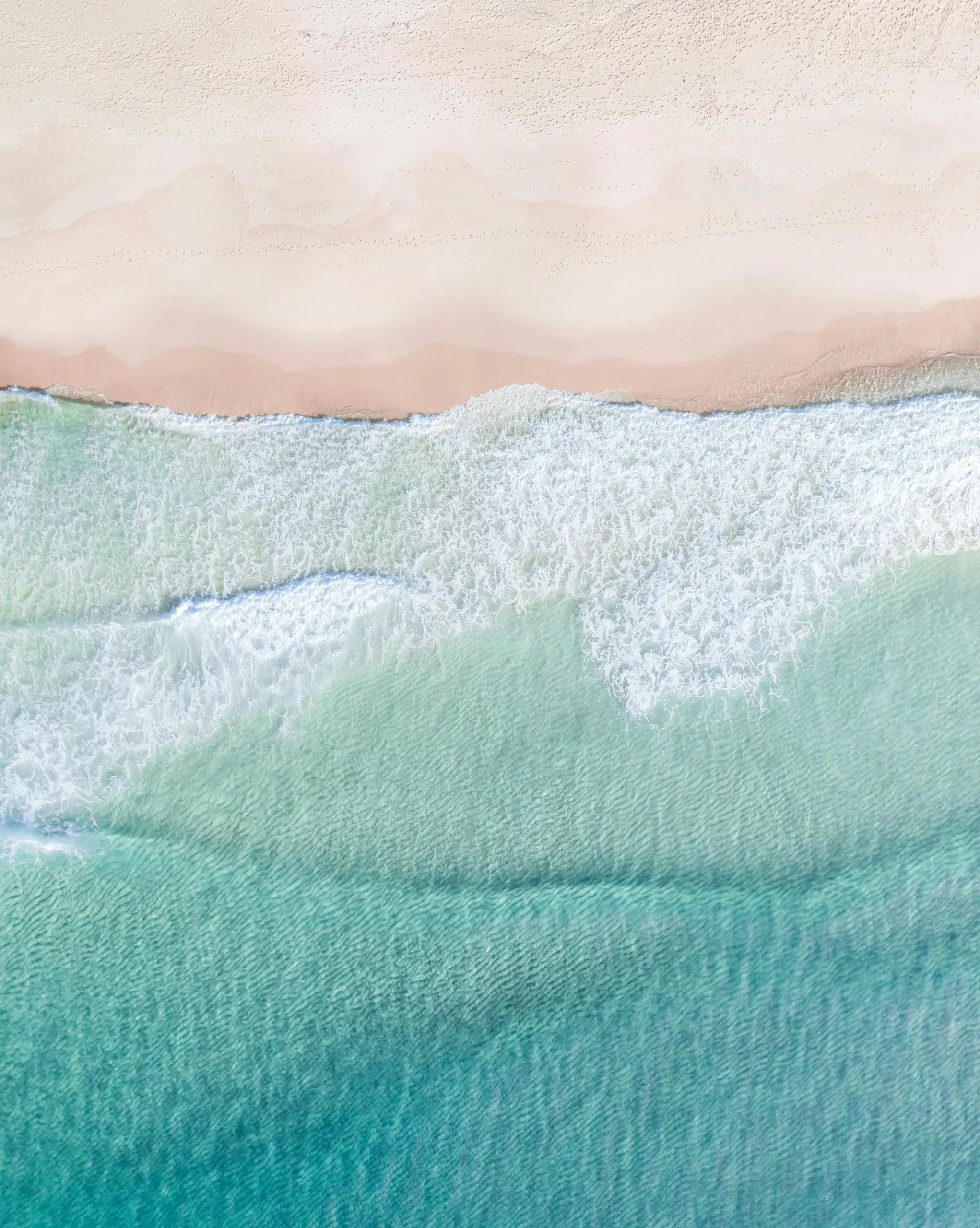 Vue aérienne d’une plage et de vagues turquoise, évoquant un voyage sur mesure haut de gamme entre raffinement et évasion.
